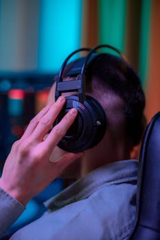 A close-up shot of a gamer wearing headphones sitting indoors in a vibrant setting.