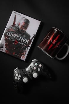 Flat lay of The Witcher Wild Hunt game with controller and themed mug on black background.