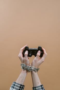 Hands chained playing video game with controller illustrating digital addiction concept.